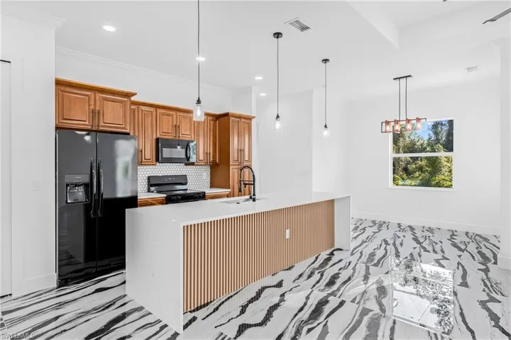 Kitchen featuring brown cabinets, black appliances, tasteful backsplash, light marble finish flooring, and pendant lighting