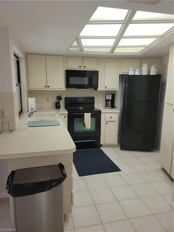 Kitchen with sink, refrigerator, black range with electric stovetop, kitchen peninsula, and cream cabinetry