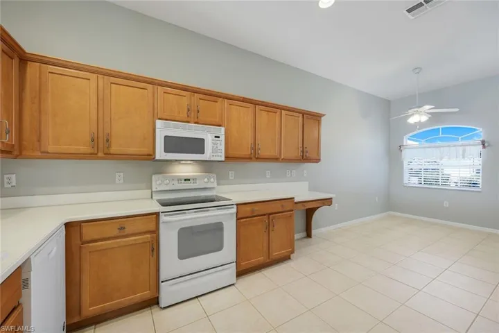 Kitchen with white appliances, brown cabinets, light countertops, and a ceiling fan