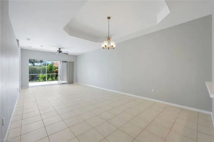 Empty room featuring a chandelier, baseboards, light tile patterned flooring, a tray ceiling, and ceiling fan