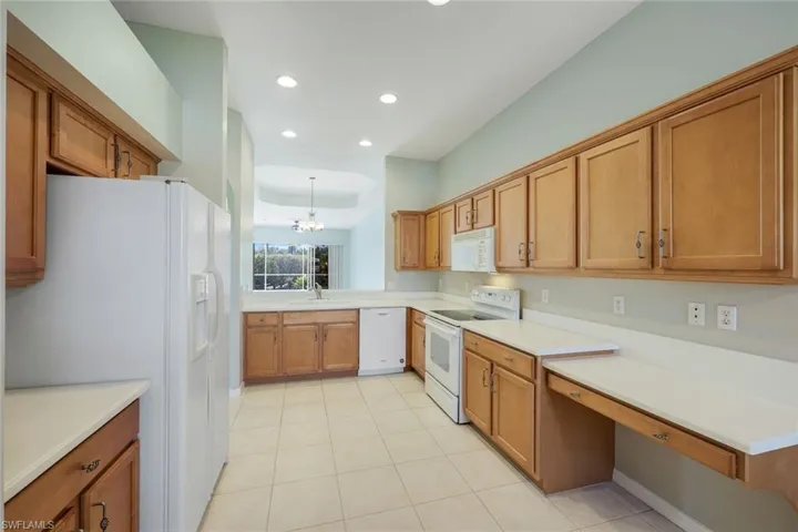 Kitchen with white appliances, a chandelier, brown cabinets, recessed lighting, and light tile patterned flooring