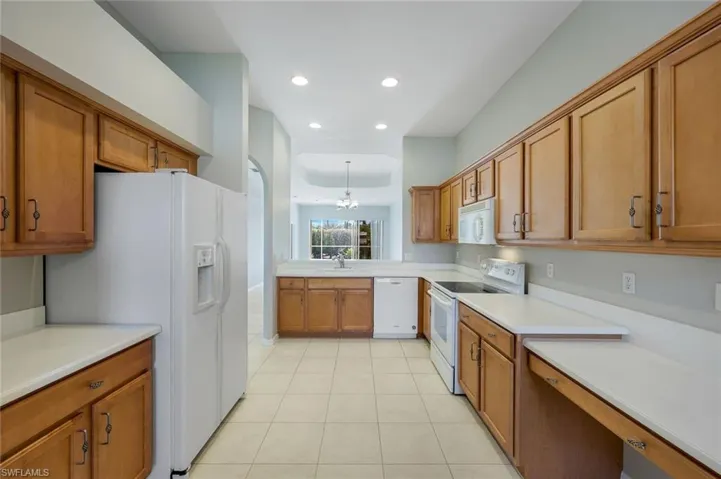 Kitchen with white appliances, brown cabinetry, light tile patterned floors, a chandelier, and light countertops
