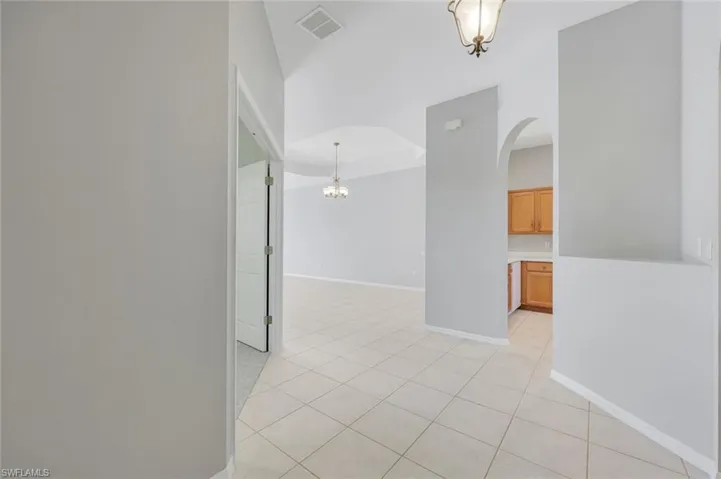 Unfurnished room with arched walkways, light tile patterned flooring, baseboards, and a chandelier