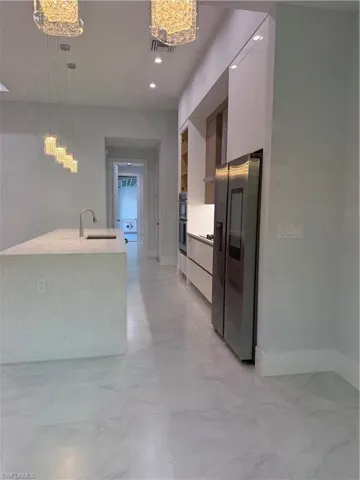 Kitchen with modern cabinets, decorative light fixtures, refrigerator, and light stone counters