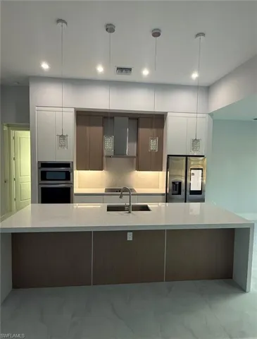 Kitchen featuring modern cabinets, light stone countertops, stainless steel appliances, a large island with sink, and decorative light fixtures