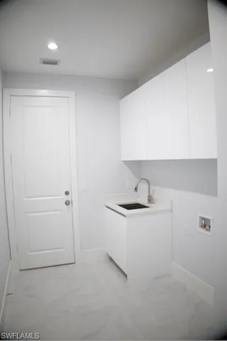 Laundry area with light marble finish flooring, cabinet space, recessed lighting, and washer hookup