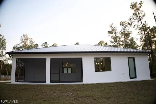 Back of property featuring a yard, stucco siding, and a standing seam roof