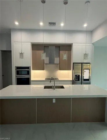 Kitchen with modern cabinets, stainless steel appliances, a large island with sink, light stone counters, and two tone color scheme