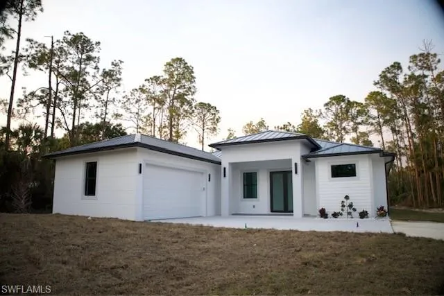 Rear view of house with an attached garage, a lawn, and a standing seam roof