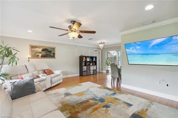 Living room with light wood-type flooring, ceiling fan, and ornamental molding