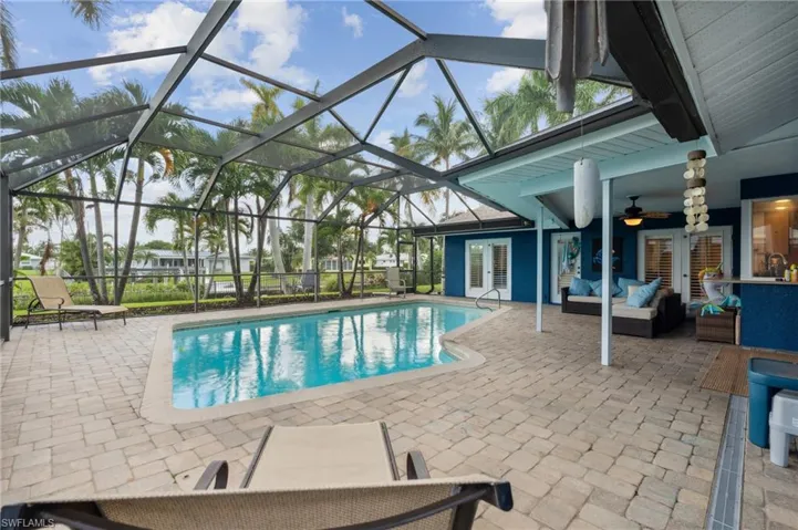 View of pool featuring glass enclosure, ceiling fan, a patio, and an outdoor living space