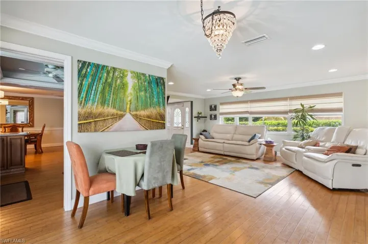 Dining room with crown molding, ceiling fan with notable chandelier, and light hardwood / wood-style floors