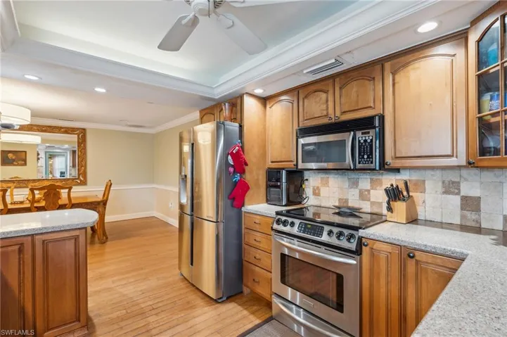 Kitchen featuring crown molding, light hardwood / wood-style flooring, appliances with stainless steel finishes, light stone counters, and ceiling fan