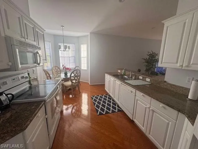 Kitchen featuring white appliances, dark stone counters, dark wood-style floors, decorative light fixtures, and a peninsula