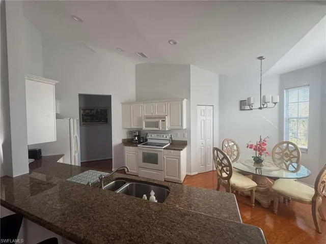 Kitchen featuring dark wood-type flooring, white appliances, hanging light fixtures, a chandelier, and white cabinets
