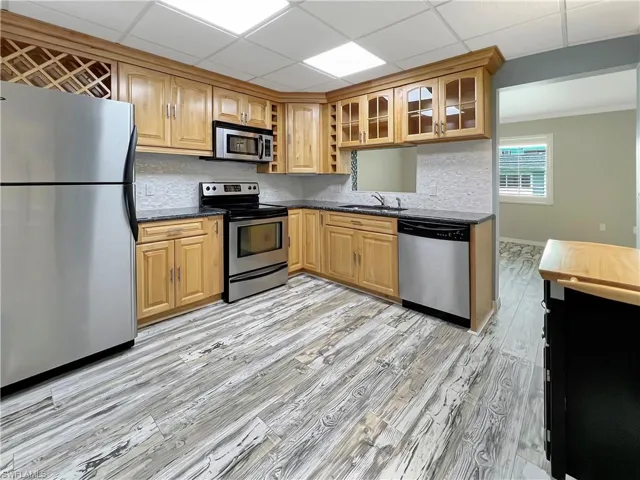 Kitchen featuring light hardwood / wood-style flooring, a paneled ceiling, dark stone countertops, sink, and appliances with stainless steel finishes