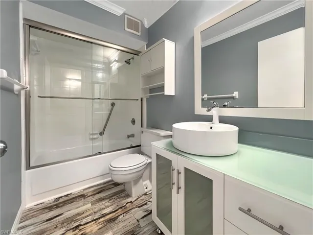 Full bathroom featuring enclosed tub / shower combo, vanity, wood-type flooring, crown molding, and toilet