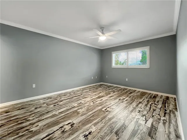 Primary bedroom featuring ceiling fan, hardwood / wood-style flooring, and crown molding