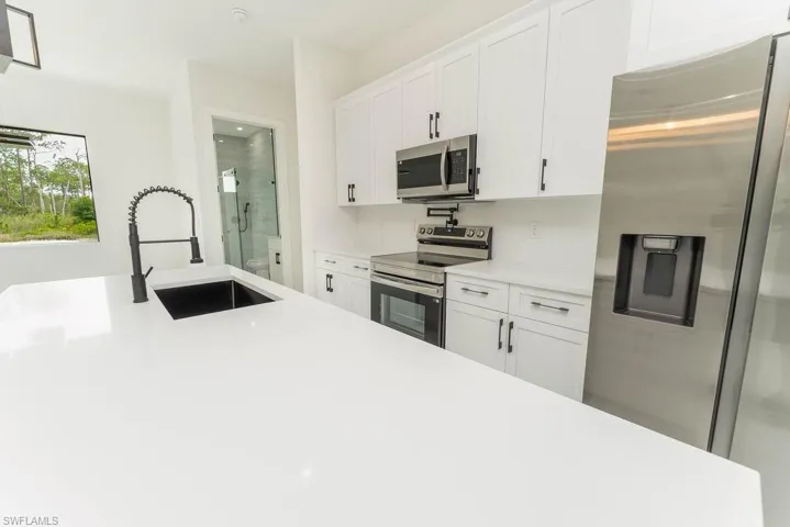 Kitchen with appliances with stainless steel finishes, a sink, light countertops, and white cabinetry