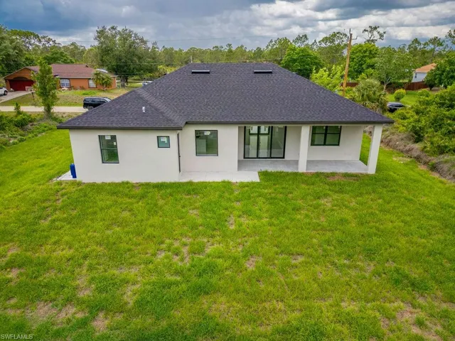 Back of house featuring a shingled roof, a patio area, stucco siding, and a lawn