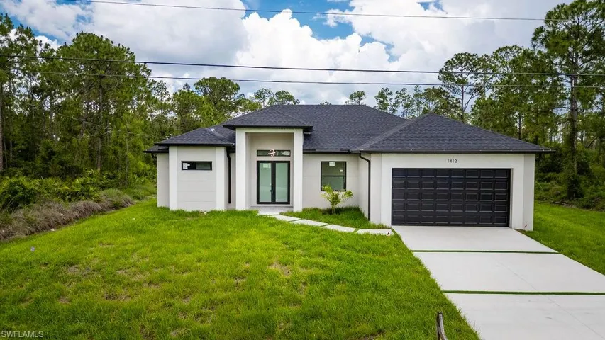 View of front of house featuring stucco siding, a garage, a front yard, driveway, and roof with shingles