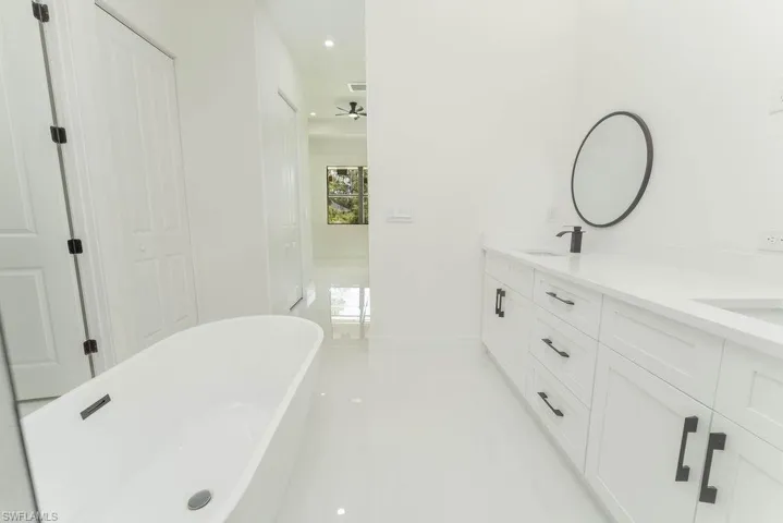 Bathroom featuring a soaking tub, double vanity, baseboards, a ceiling fan, and recessed lighting