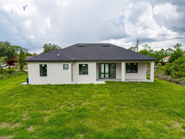 Back of house featuring a patio area, stucco siding, roof with shingles, and a yard