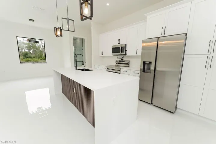 Kitchen with appliances with stainless steel finishes, a sink, white cabinets, light tile patterned flooring, and light countertops