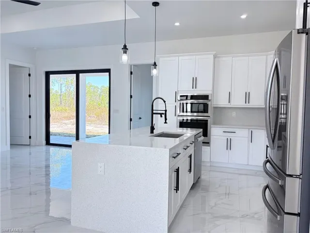 Kitchen with a sink, marble finish floor, appliances with stainless steel finishes, light stone countertops, and pendant lighting