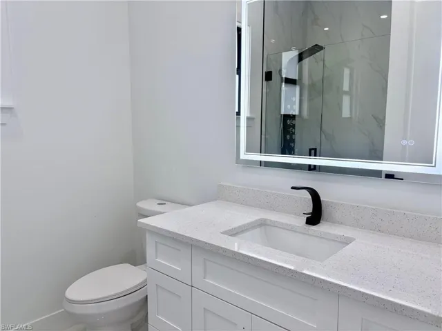 Bathroom with a marble finish shower, vanity, and toilet