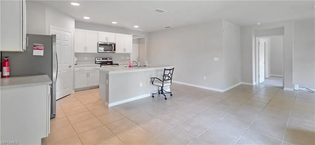 Open-concept kitchen and living area featuring tile flooring, white cabinetry, stainless steel appliances, and an island with a breakfast bar