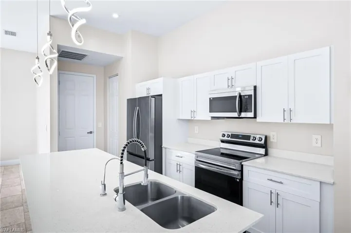 Kitchen with stainless steel appliances, white cabinets, and light stone counters