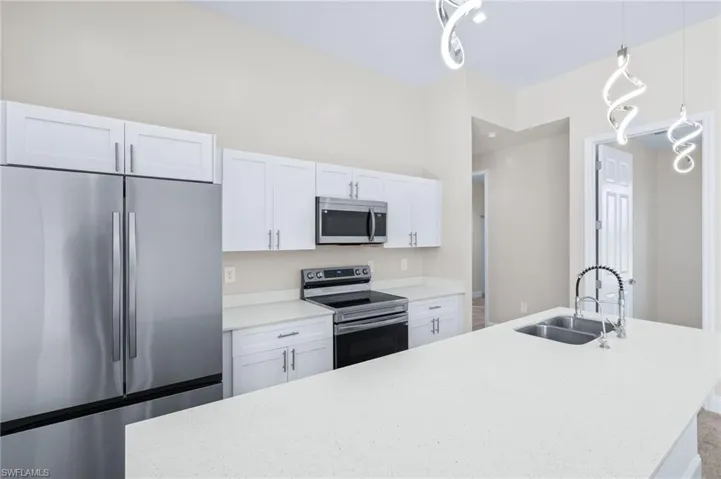 Kitchen featuring stainless steel appliances, white cabinetry, a center island with sink, hanging light fixtures, and light stone counters