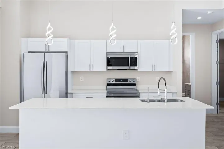 Kitchen with white cabinets, stainless steel appliances, light stone counters, and hanging light fixtures
