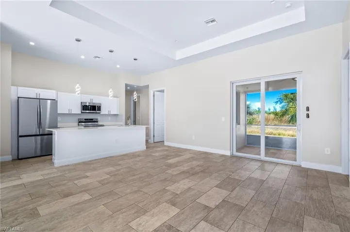 Kitchen with stainless steel appliances, white cabinets, an island with sink, pendant lighting, and open floor plan