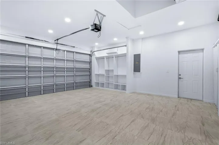 Garage with electric panel, recessed lighting, and a garage door opener