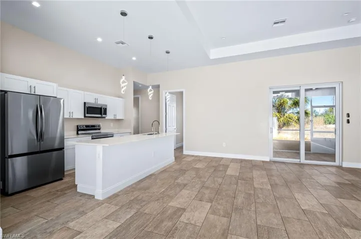 Kitchen with stainless steel appliances, white cabinets, decorative light fixtures, an island with sink, and light stone counters