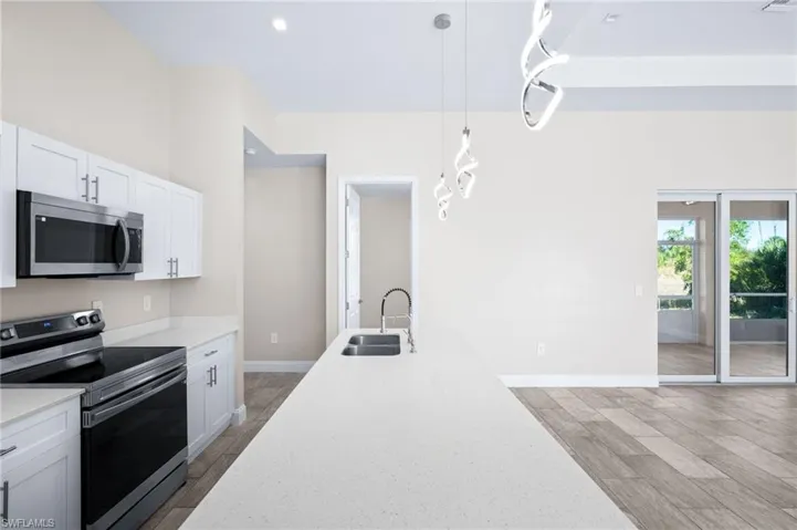 Kitchen featuring stainless steel appliances, hanging light fixtures, white cabinetry, light stone counters, and wood tiled floors