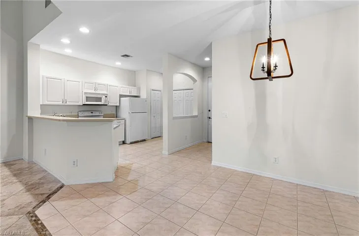 Kitchen featuring recessed lighting, a peninsula, white cabinets, white appliances, and a kitchen bar