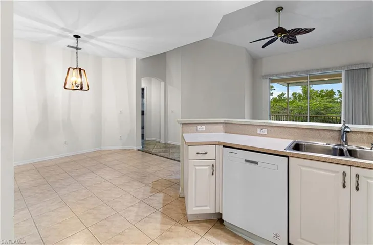 Kitchen with dishwasher, white cabinetry, light countertops, pendant lighting, and arched walkways