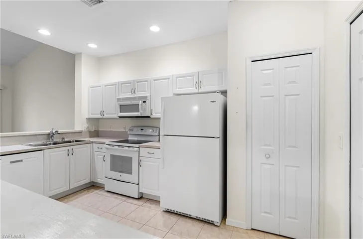 Kitchen featuring white appliances, white cabinets, light countertops, light tile patterned floors, and recessed lighting