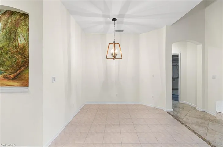 Unfurnished dining area with arched walkways, light tile patterned floors, a chandelier, and inlaid floor details