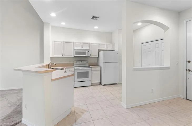 Kitchen featuring white appliances, a peninsula, light countertops, white cabinets, and recessed lighting