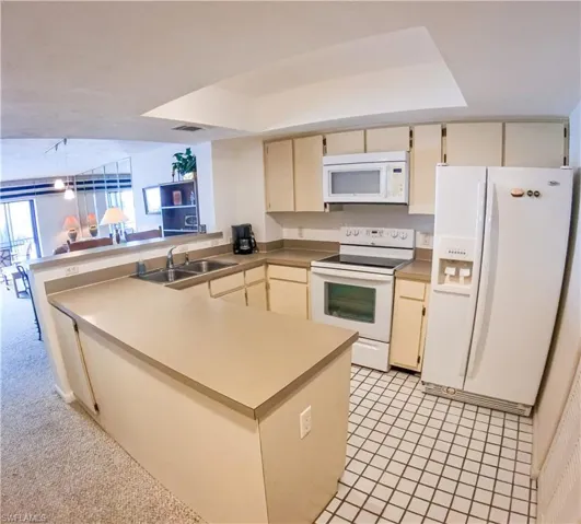 Kitchen with white appliances, sink, cream cabinetry, a raised ceiling, and kitchen peninsula