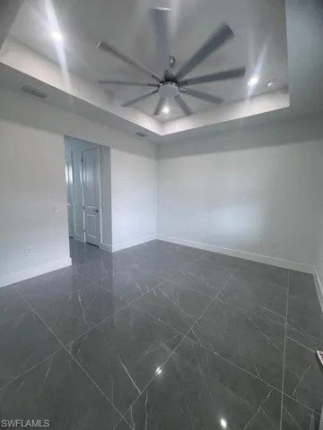 Spare room with a raised ceiling, baseboards, dark marble finish floors, and ceiling fan