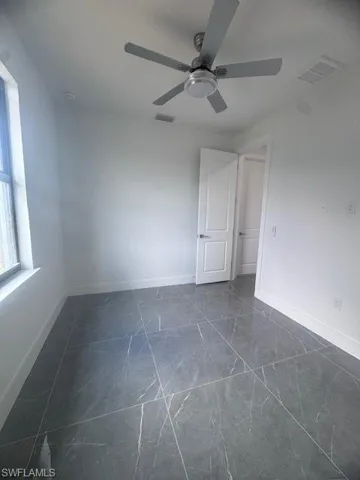 Unfurnished room with baseboards, a ceiling fan, and dark marble finish flooring