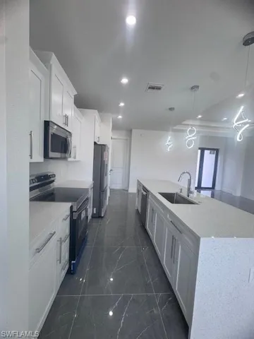 Kitchen featuring range, a sink, fridge, a large island with sink, and white cabinetry
