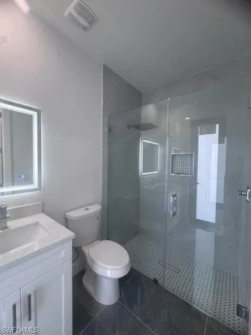Full bathroom with vanity, a shower stall, toilet, and marble finish floors