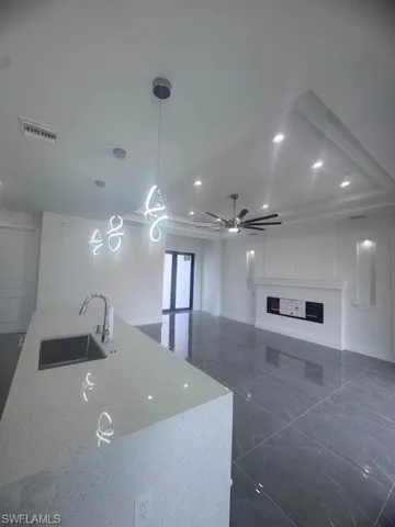Kitchen with a sink, a fireplace, open floor plan, hanging light fixtures, and light stone counters