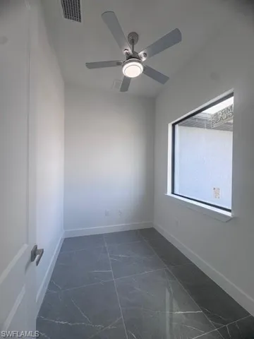 Spare room featuring dark marble finish floors, a ceiling fan, and baseboards